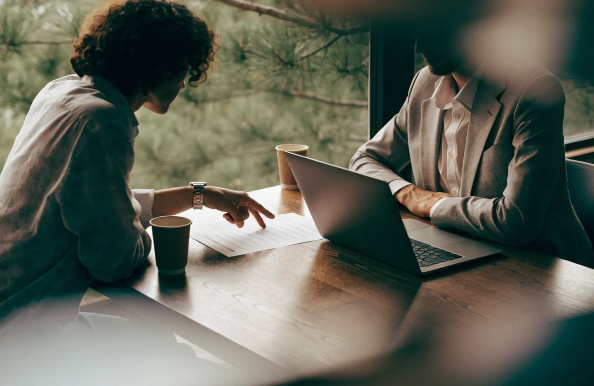 Two professionals reviewing a printed checklist and a laptop across a wooden table