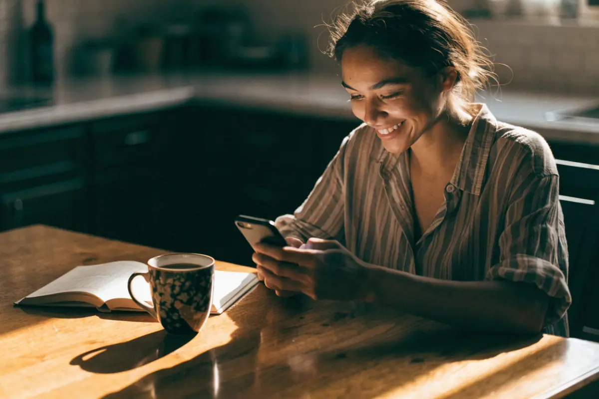 A woman opening an email offer on her phone over morning coffee