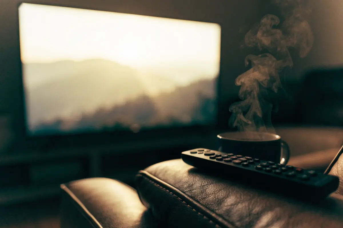 A smart TV glowing in a dark living room, a remote on the armrest