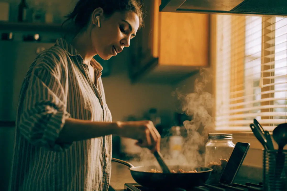 A woman listening on earbuds while cooking dinner