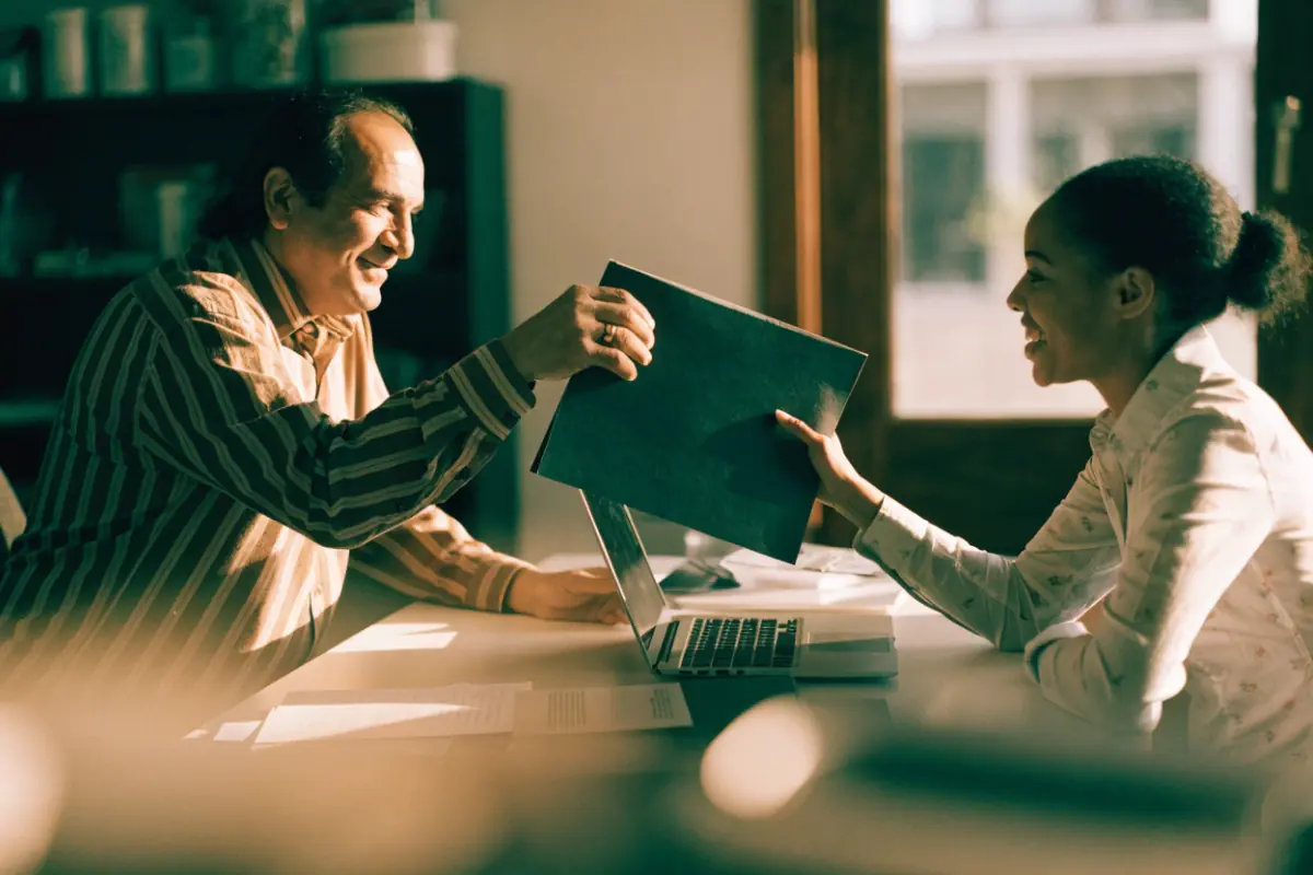 A business owner handing a plan to a marketing specialist across a desk