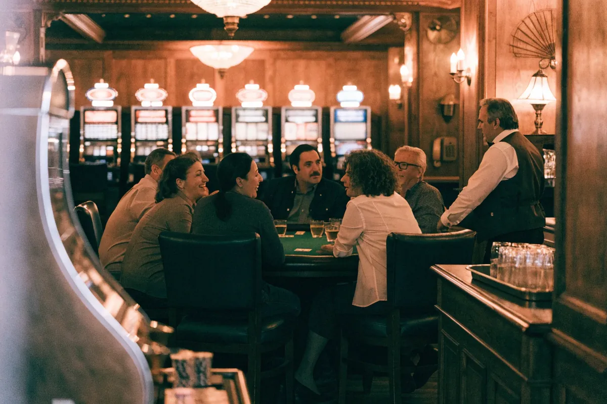 Adults laughing at a blackjack table in a historic wood-paneled casino with slot machines behind