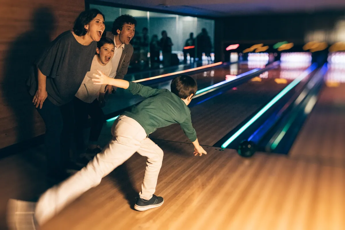 A family cheering as a boy bowls under neon lane lights