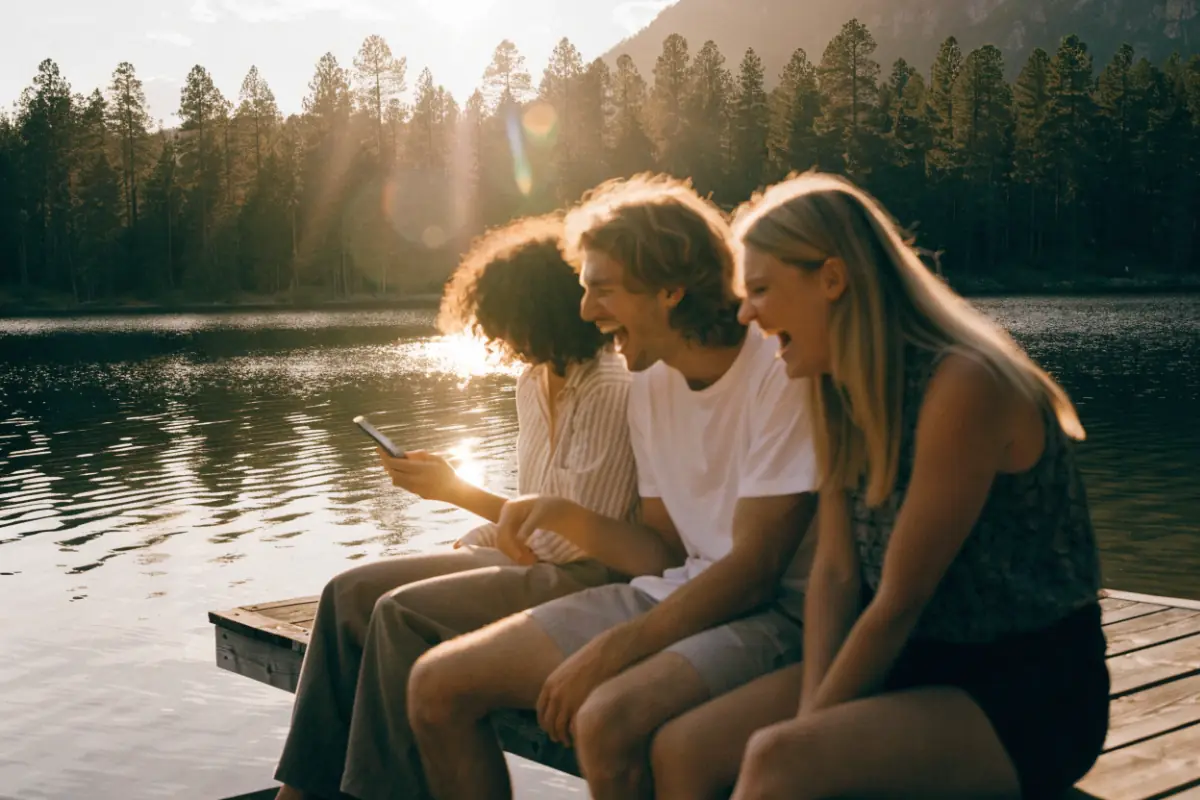 Friends laughing at something on a phone on a lake dock at sunset