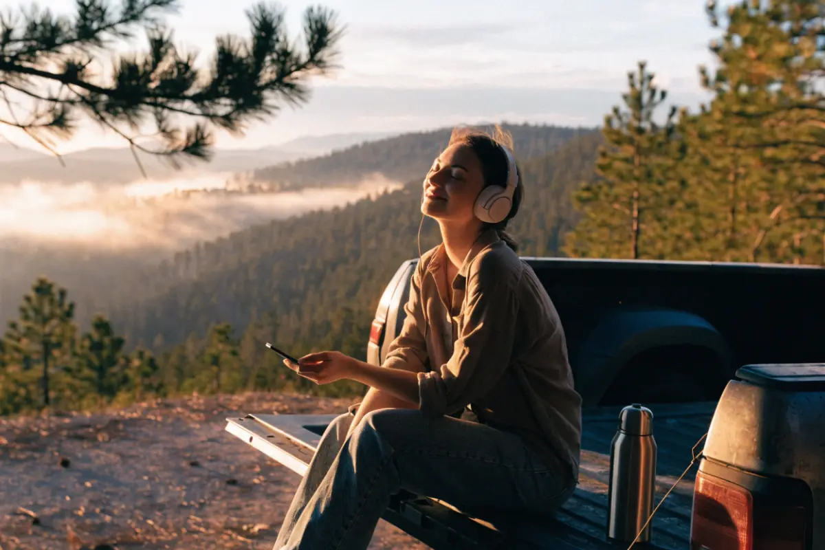 A woman in headphones on a truck tailgate at a misty mountain overlook at sunrise